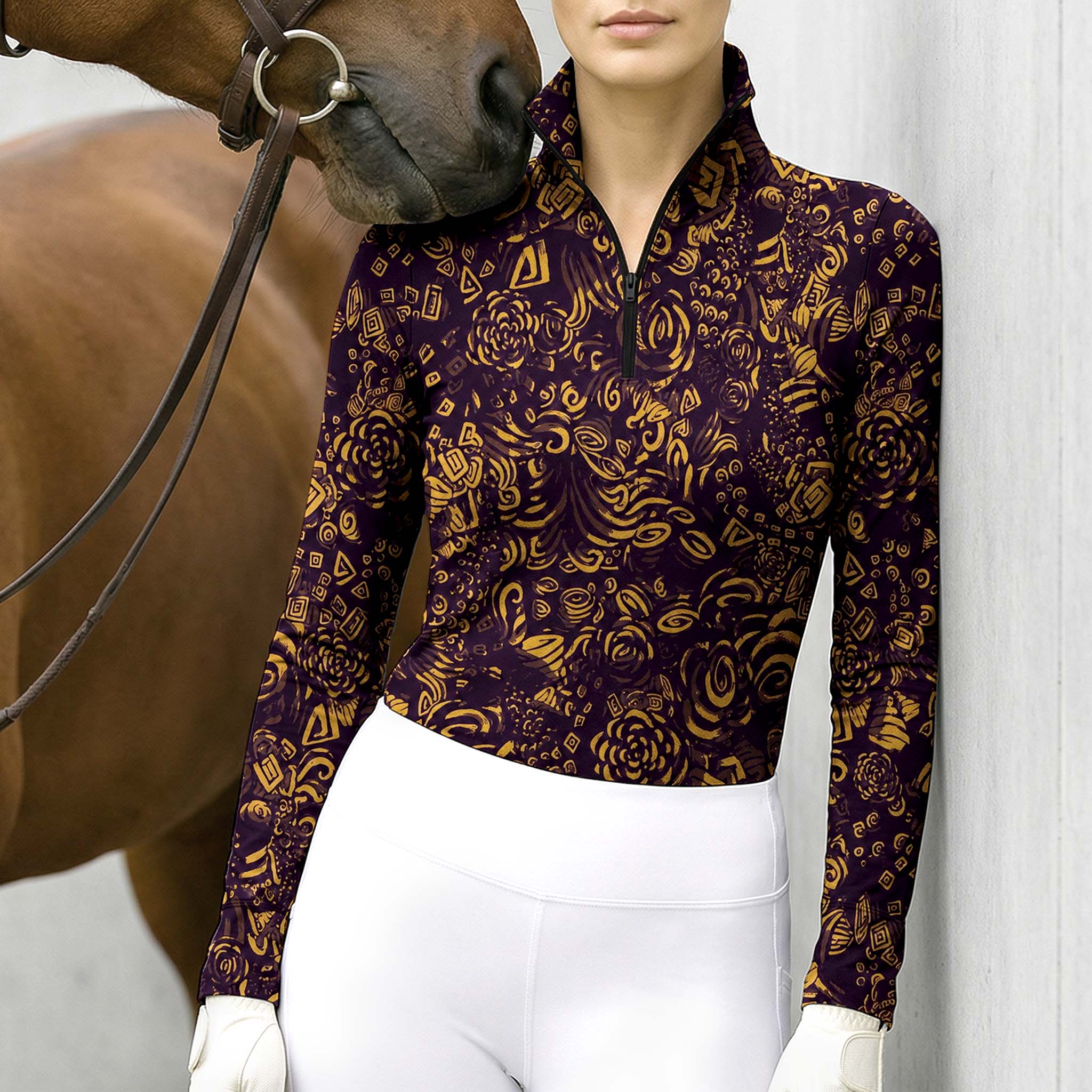 Outdoor wall‑side lifestyle shot of female equestrian leaning against wall beside brown horse, wearing deep‑purple golden doodle‑print long‑sleeve riding top and white riding breeches