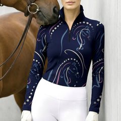 Competition venue close‑up shot of female rider wearing navy‑blue pastel multi‑line‑art horse‑print long‑sleeve quarter‑zip riding top and white breeches