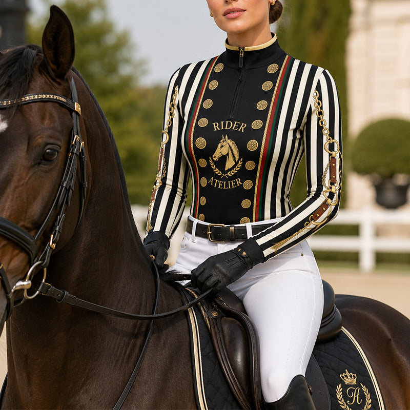 Outdoor lifestyle shot of female equestrian beside white horse wearing black‑white stripe vintage military‑style graphic long‑sleeve riding top and white riding breeches