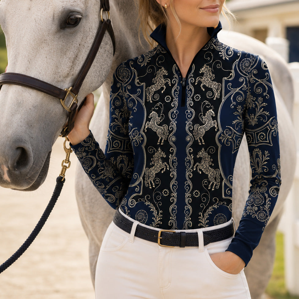 Ranch outdoor casual shot of female rider leaning on white wooden fence, wearing navy‑black vintage golden carousel‑horse scroll‑filigree print riding top, white breeches and black belt