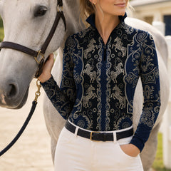 Ranch outdoor casual shot of female rider leaning on white wooden fence, wearing navy‑black vintage golden carousel‑horse scroll‑filigree print riding top, white breeches and black belt