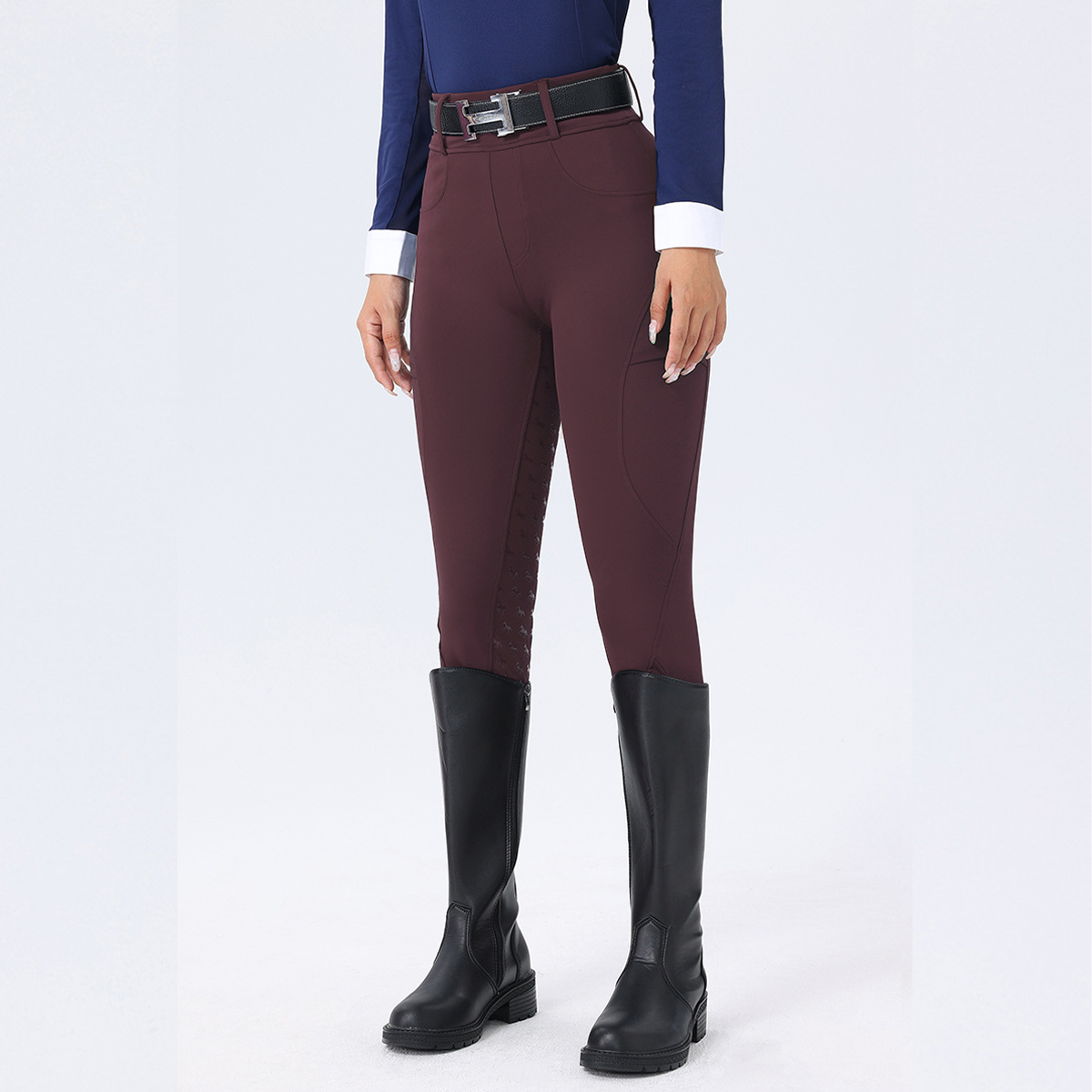 Person wearing maroon riding pants with black boots on a white background
