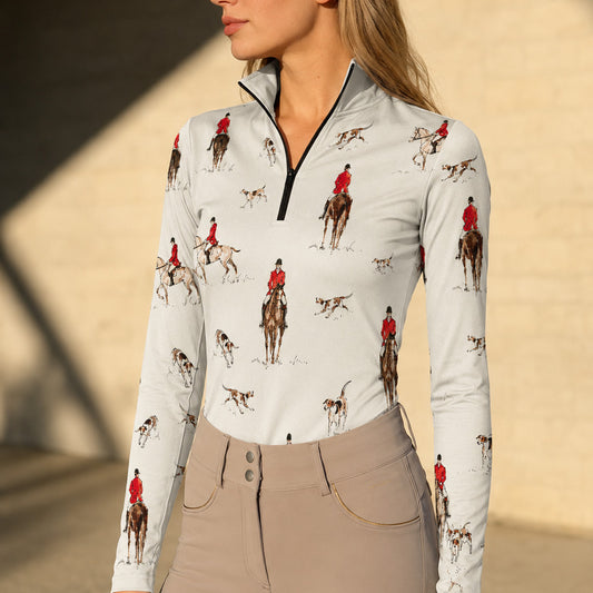 Sunny stone wall lifestyle shot of female equestrian wearing cream vintage fox‑hunting rider hound dog watercolor print long‑sleeve riding top paired with taupe riding breeches