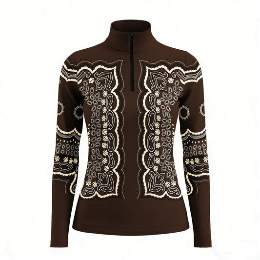 Outdoor garden lifestyle shot of female equestrian wearing chocolate‑brown vintage bandana‑paisley print long‑sleeve riding top beside wild daisy flower beds, paired with navy riding breeches