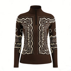 Outdoor garden lifestyle shot of female equestrian wearing chocolate‑brown vintage bandana‑paisley print long‑sleeve riding top beside wild daisy flower beds, paired with navy riding breeches