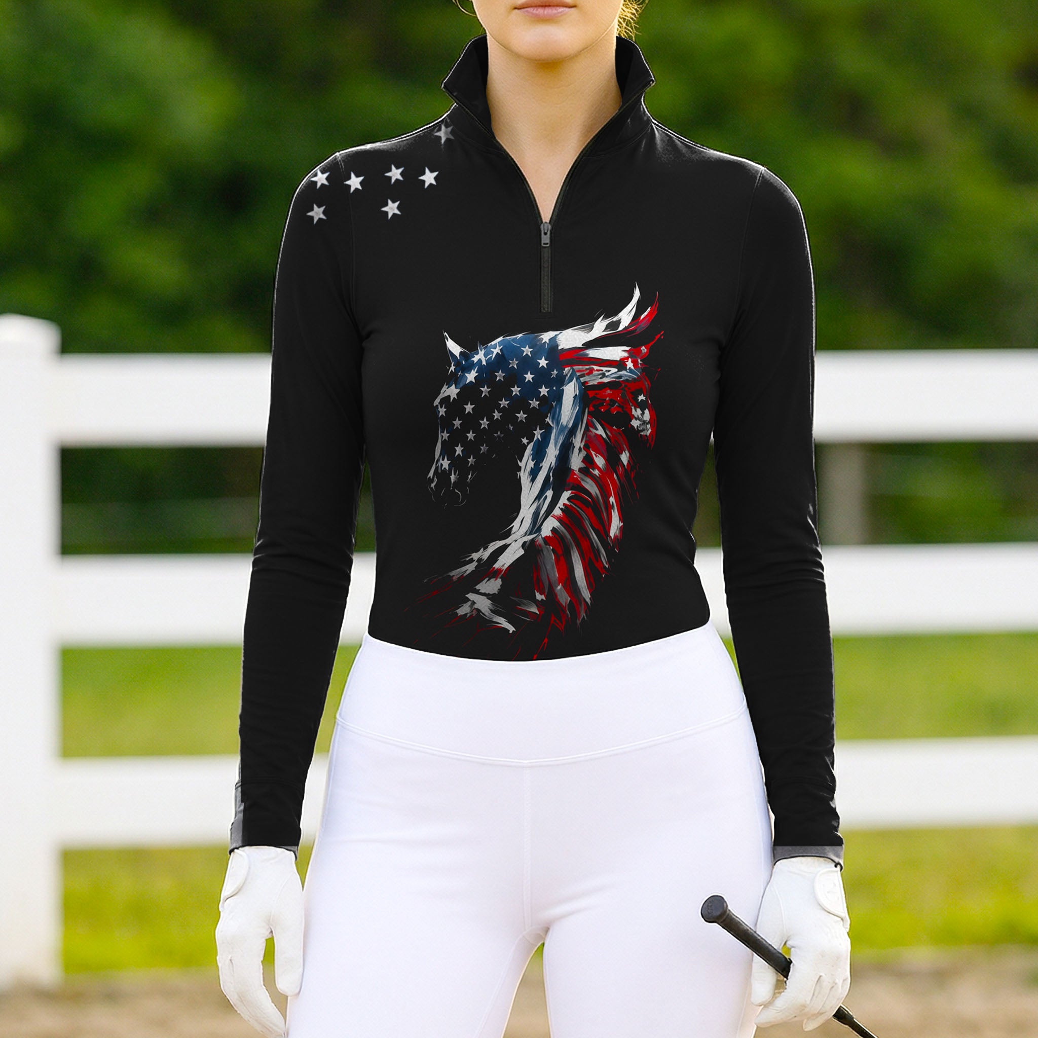 Model wearing the American Flag Horse Head Print Riding Top at an outdoor equestrian arena, with jumps in the background
