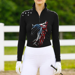Model wearing the American Flag Horse Head Print Riding Top at an outdoor equestrian arena, with jumps in the background
