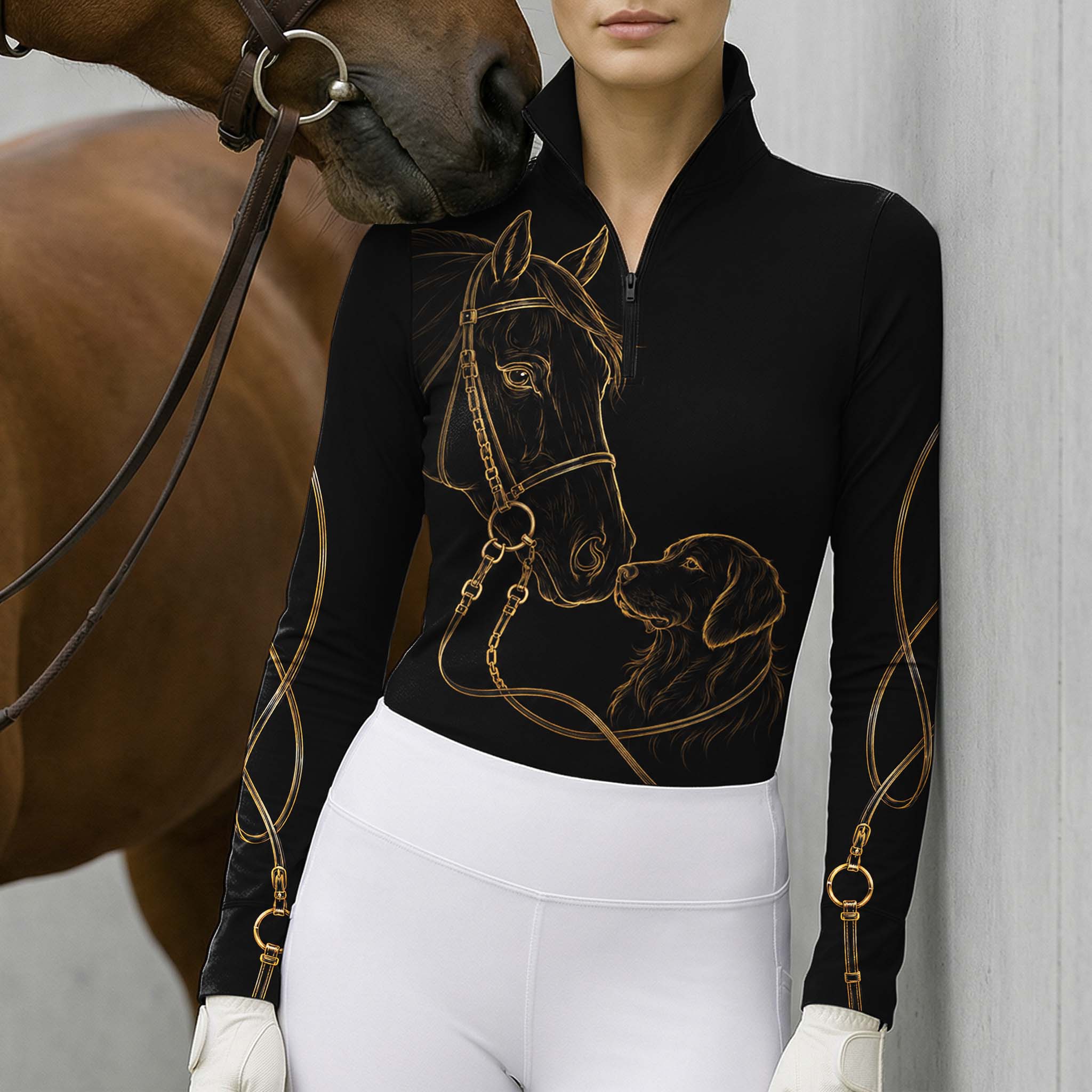 Model standing beside brown horse’s head wearing black gold line art horse & golden retriever long sleeve riding top against light grey stable wall
