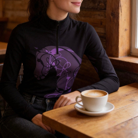 Warm wooden indoor cafe shot of female equestrian seated wearing black base abstract purple line art sitting horse print long sleeve quarter-zip riding top