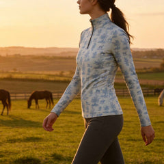 Sunset golden hour countryside pasture lifestyle shot of model walking among grazing horses in vintage blue toile equestrian riding top
