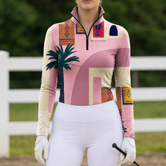 Sunlit green pasture white rail fence shot of model holding white riding gloves showcasing warm boho coastal tropical palm geometric abstract equestrian long sleeve top
