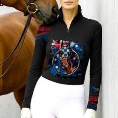 Woman wearing RIDER ATELIER Australian Flag Racehorse Top in Classic Black, leaning against a stable wall with a chestnut horse nuzzling her shoulder, showing the print’s high contrast
