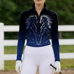 Model wearing the Constellation Twin Horses Print Riding Top at an outdoor equestrian arena, with jumps in the background
