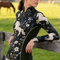 Outdoor grass pasture wooden rail fence shot of female rider leaning on fence wearing dark wildflower white unicorn all-over print long sleeve quarter-zip riding top with olive side panels