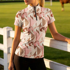 Warm golden hour grass pasture white wooden rail fence shot of female equestrian leaning on fence wearing blush taupe abstract geometric brushstroke horse head all-over print short sleeve riding top and black riding breeches