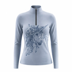 Close-up shot of model’s hand adjusting black half-zip stand collar of solid blue boho unicorn sketch long sleeve riding top in green grass pasture
