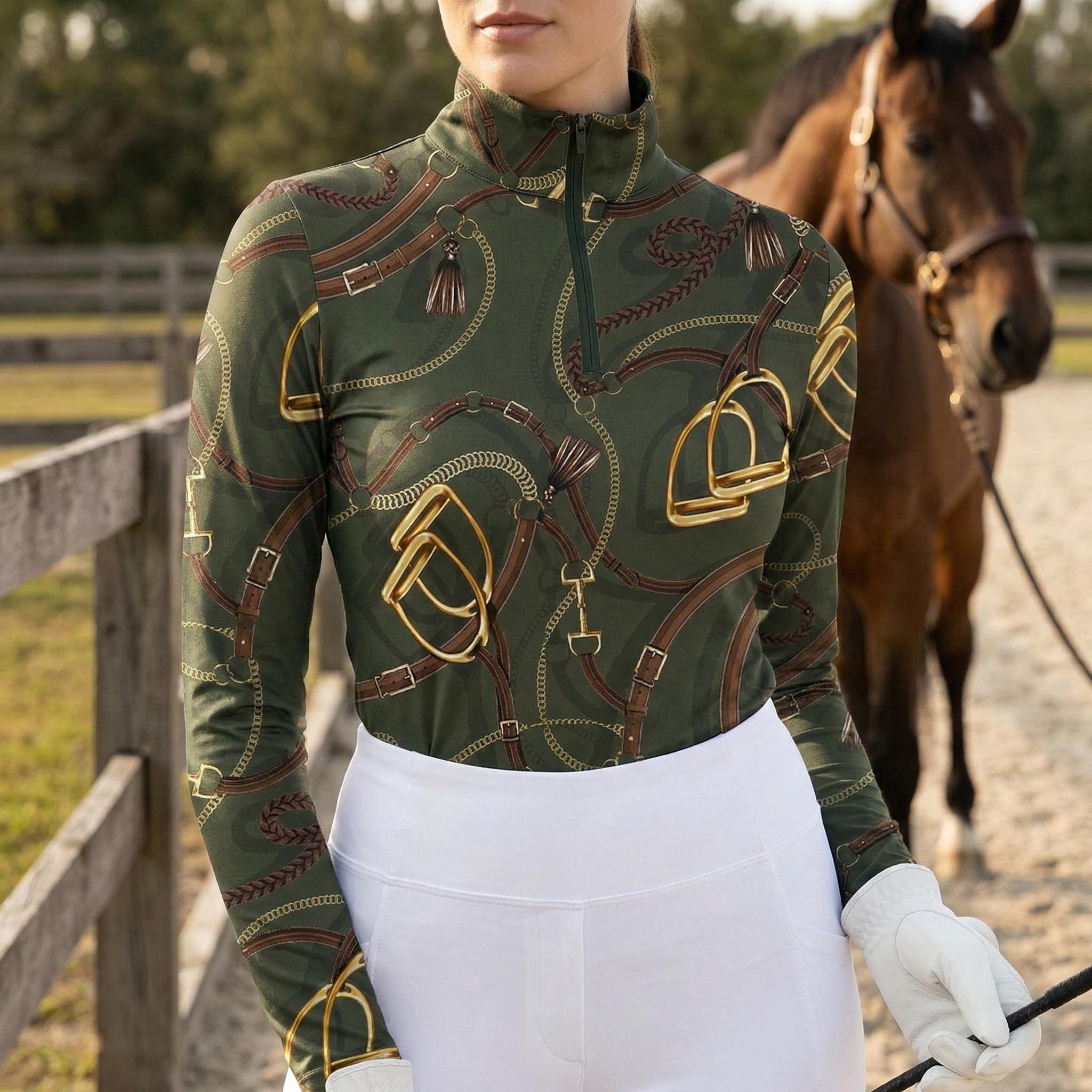 Woman wearing olive equestrian tack and tassel print long sleeve zip top standing beside a horse at the stable