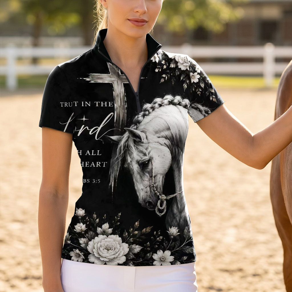 Model standing beside chestnut horse at sunlit dirt riding arena wearing spiritual dark floral horse cross short sleeve riding top
