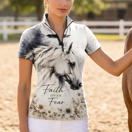 Model standing beside chestnut horse at sunlit dirt riding arena wearing soft vintage spiritual watercolor horse cross short sleeve riding top
