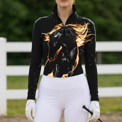 Full-body model shot wearing dramatic wild fiery horse long sleeve top at sunlit green pasture white wooden fence, holding riding crop
