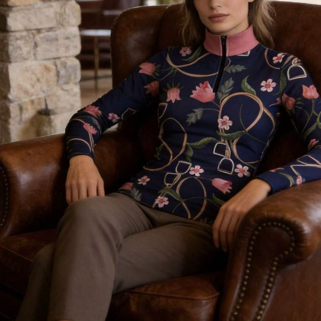 Model wearing navy floral & stirrup print riding top seated in a leather armchair