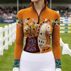 Sunlit equestrian competition show jumping arena shot of model wearing vibrant orange folk art spotted cream horse floral golden berry decorative green scroll cuff riding top
