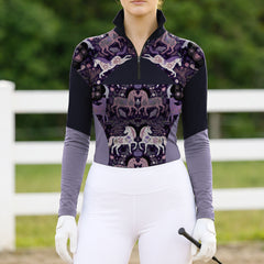 Full-body model shot wearing moody folk art color block equestrian riding top at sunlit green pasture white wooden fence, holding riding crop