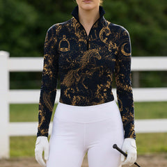 Sunlit sandy arena shot of model standing beside a horse showcasing the slim tailored fit and luminous golden celestial equestrian full print
