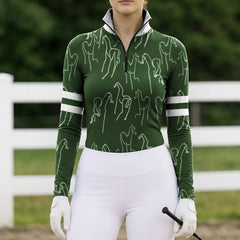Full-body model shot wearing timeless forest green equestrian long sleeve top at sunlit green pasture white wooden fence, holding riding crop
