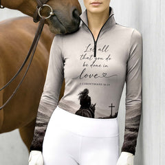 Model leaning against light grey stable wall beside chestnut horse wearing gradient grey bible verse mountain rider riding top

