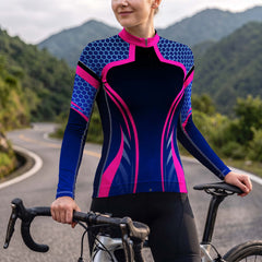 Female model wearing navy pink hexagon streamline long sleeve bike jersey riding road bike on winding mountain trail, front torso view
