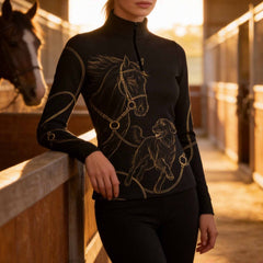 Lifestyle shot of female model leaning on stable rail, wearing black gold line‑art horse and retriever dog long‑sleeve quarter‑zip riding top