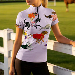 Side model shot leaning on white wooden pasture fence wearing soft pale lavender base multi-breed dog sweater watercolor short sleeve riding top in sunlit green grass field
