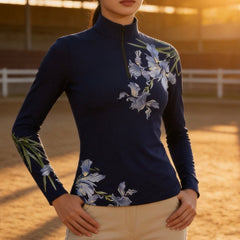 Outdoor tree‑shade pasture lifestyle close‑up of rider wearing lavender iris floral long‑sleeve riding top