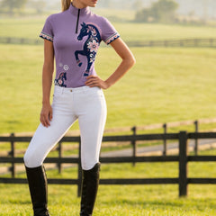 Full-body model shot wearing lilac folk floral horse riding top in sunlit green pasture with black fencing