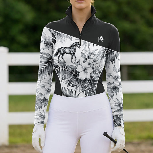 Model wearing the Monochrome Tropical Horse Print Riding Top at an outdoor equestrian arena, with jumps in the background
