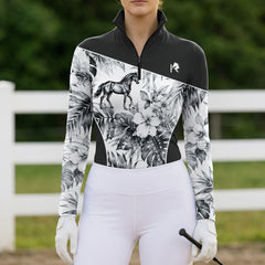 Model wearing the Monochrome Tropical Horse Print Riding Top at an outdoor equestrian arena, with jumps in the background
