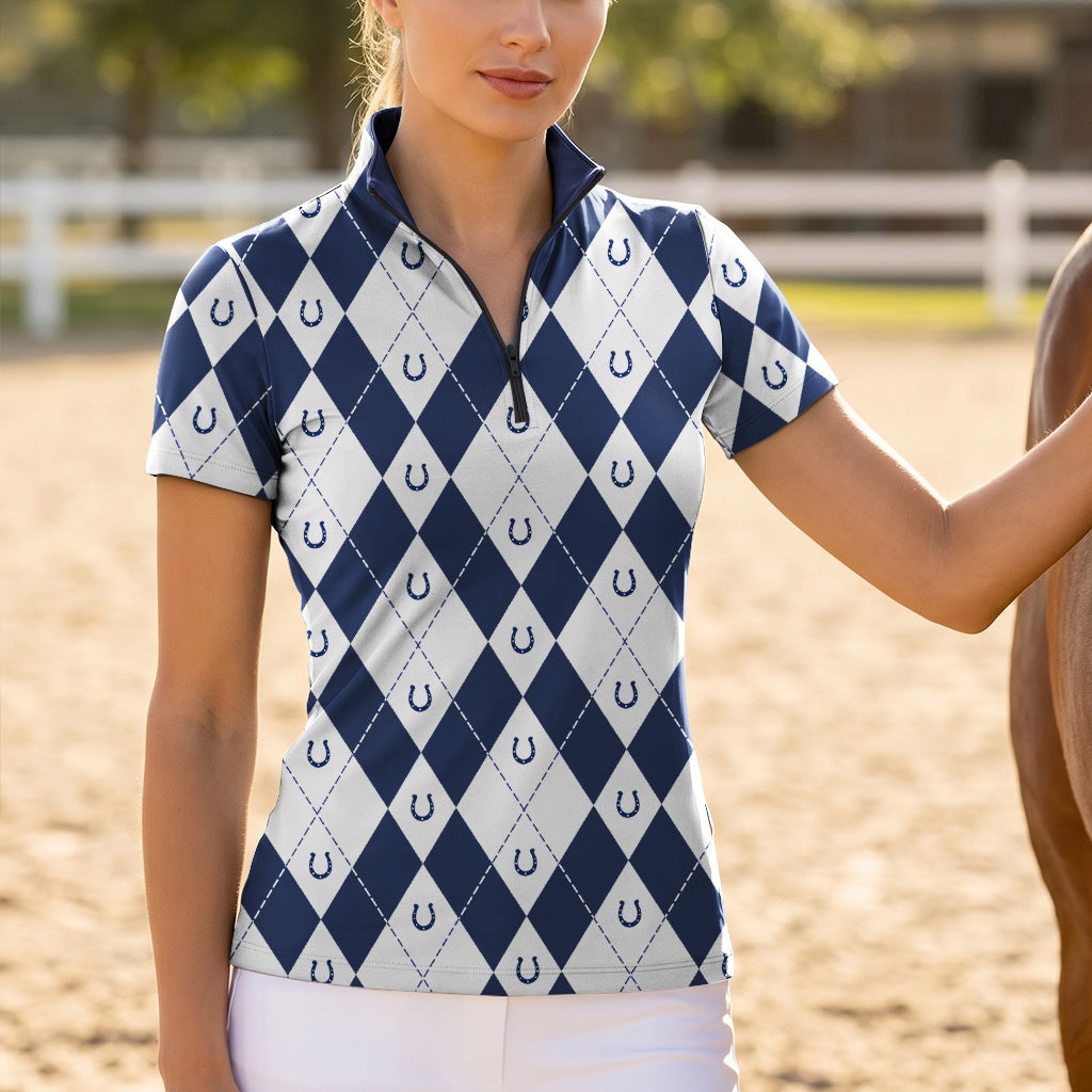 Model wearing the navy version of the Argyle & Horseshoe Print Short-Sleeve Riding Top at the stable, with a chestnut horse
