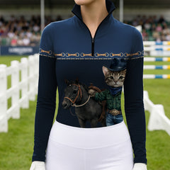 Equestrian show‑jumping arena close‑up model shot of rider in navy quarter‑zip long‑sleeve riding top with cowboy cat pony print