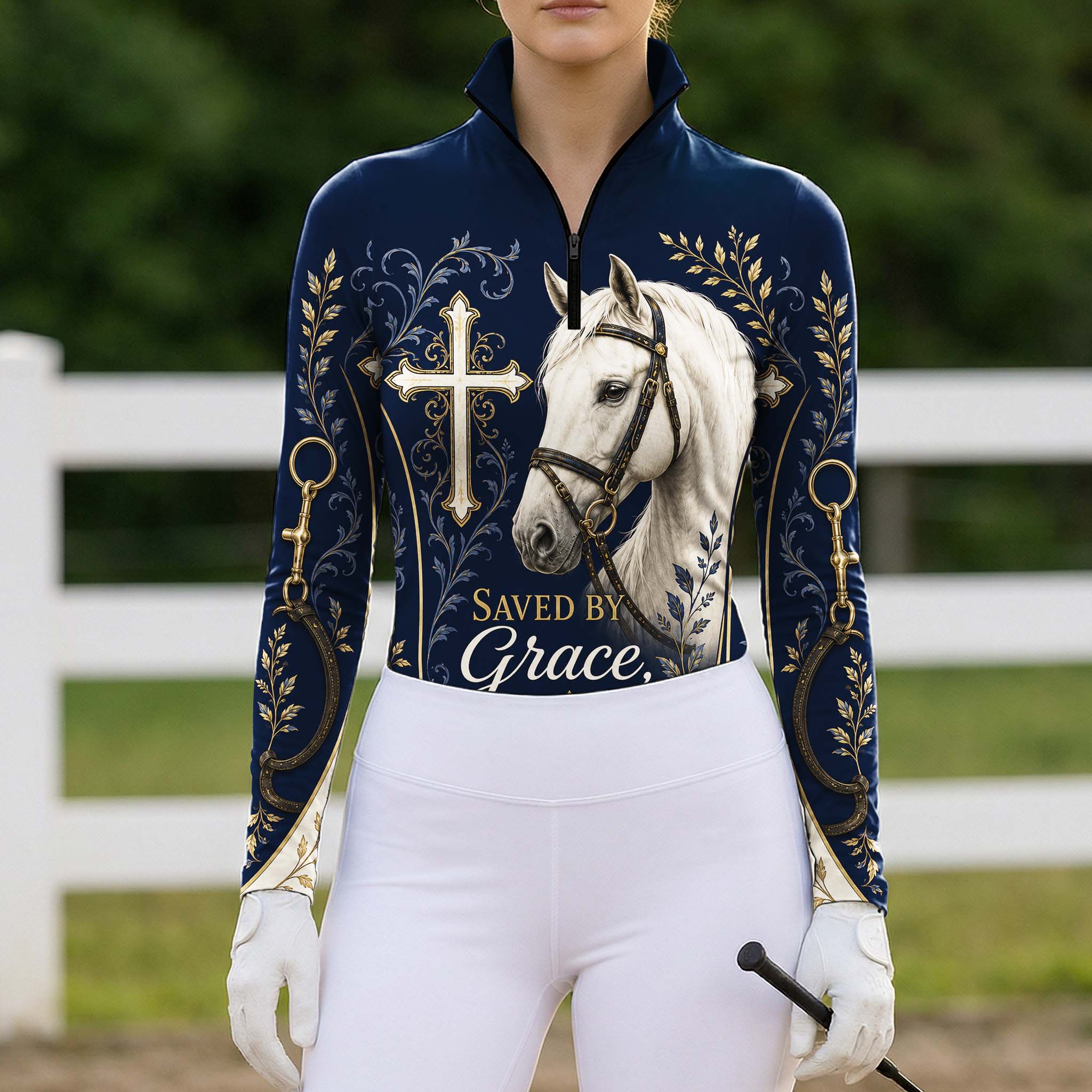 Full-body model shot wearing heartfelt navy faith cross horse gold scroll long sleeve riding top at outdoor equestrian show jumping arena with spectator stands, holding riding crop
