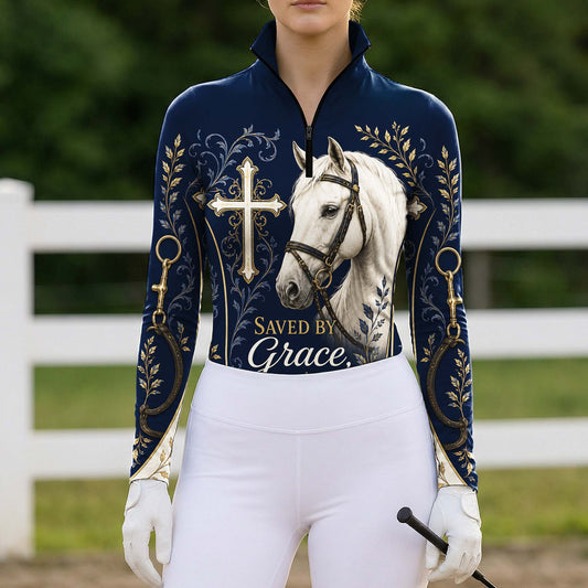 Full-body model shot wearing heartfelt navy faith cross horse gold scroll long sleeve riding top at outdoor equestrian show jumping arena with spectator stands, holding riding crop
