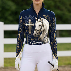 Full-body model shot wearing heartfelt navy faith cross horse gold scroll long sleeve riding top at outdoor equestrian show jumping arena with spectator stands, holding riding crop
