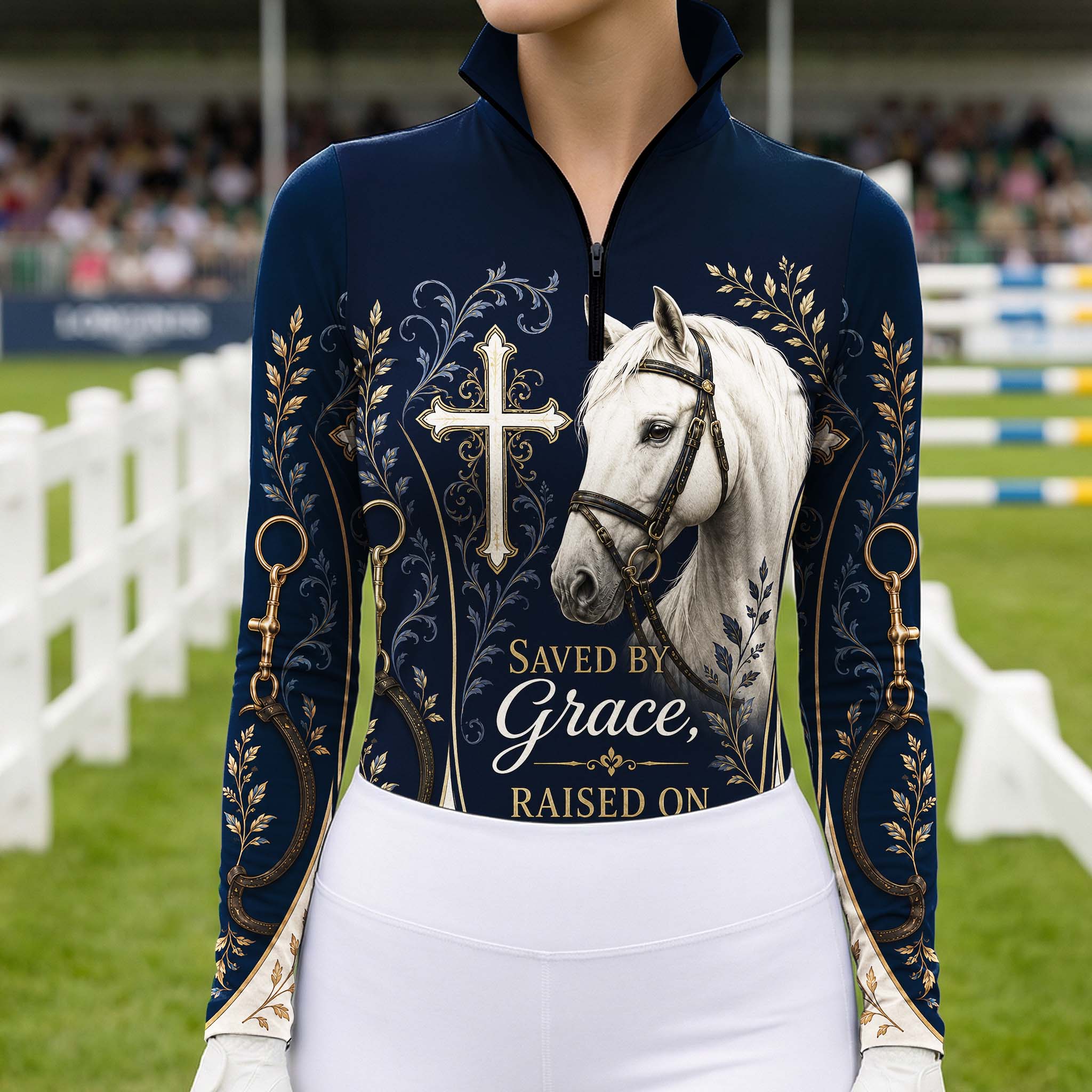 Model standing beside brown horse’s head wearing deep navy Saved By Grace cross white horse gold foliage horse bit long sleeve riding top against light grey stable wall
