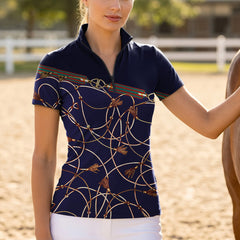 Outdoor riding arena lifestyle shot of female model wearing navy horse‑bit chain tassel print short‑sleeve riding top beside horse