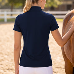 Outdoor equestrian arena rear view shot of model wearing solid back navy tack print short sleeve riding top beside horse