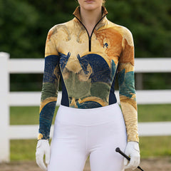 Outdoor pasture white‑fence lifestyle shot of female model wearing ochre‑gold fresco war‑horse art‑print long‑sleeve riding top