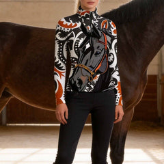 Model standing beside dark brown horse inside sunlit wooden stable wearing black white rust paisley central horse portrait long sleeve riding top