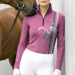Model wearing contemporary line art horse riding top beside a chestnut horse leaning against light grey stable wall