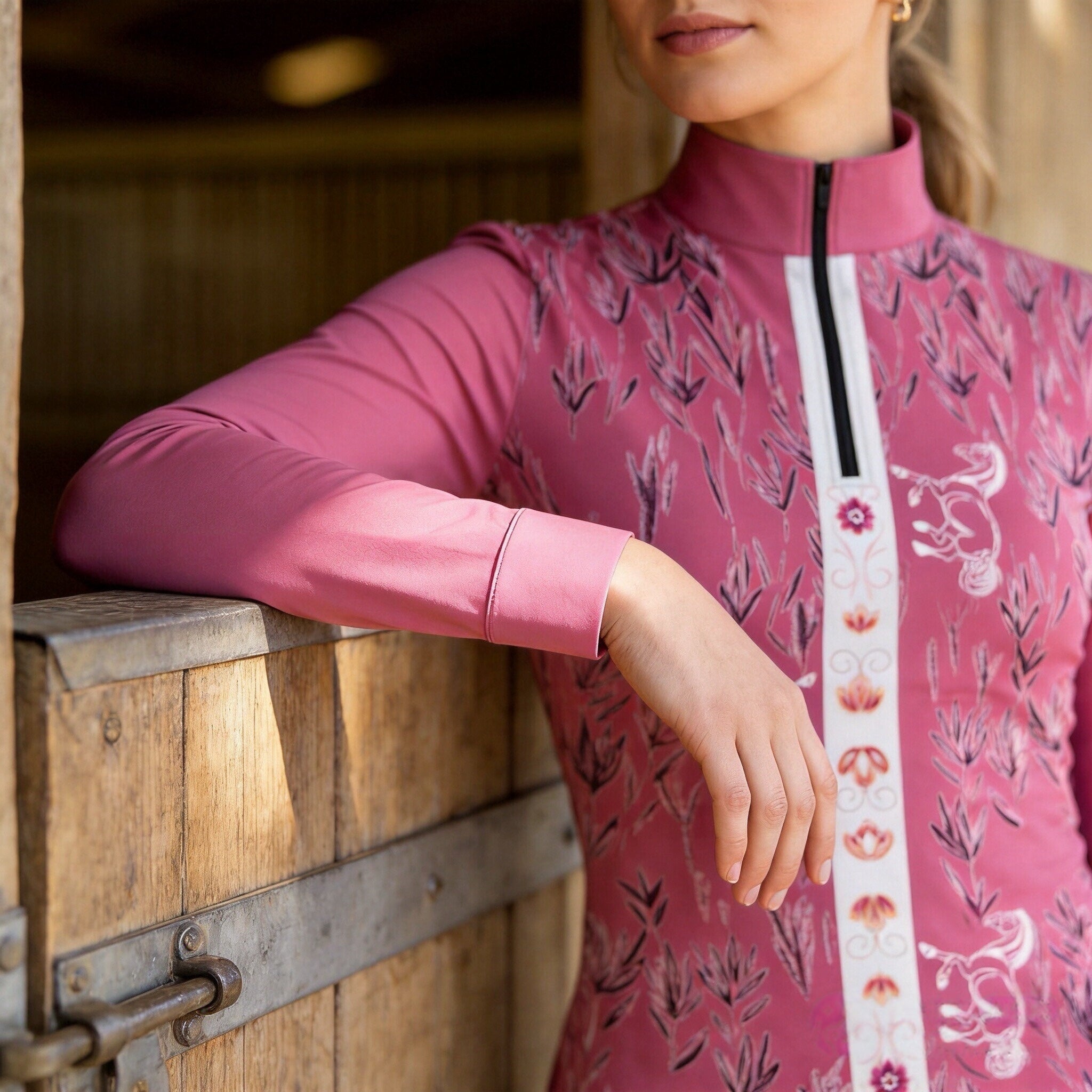 Side close-up model leaning on wooden stable stall showcasing central vertical floral horse stripe print detail on dusty pink riding top