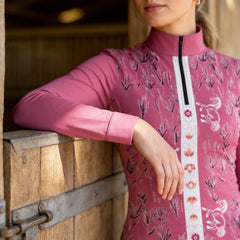 Side close-up model leaning on wooden stable stall showcasing central vertical floral horse stripe print detail on dusty pink riding top